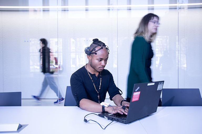 Man wearing a headset sensor while working on a laptop.