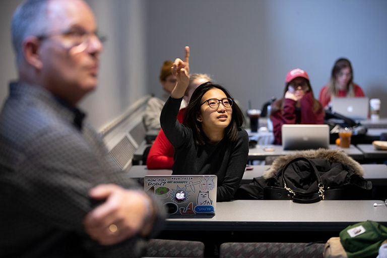 Young woman with hand raised in classroom.